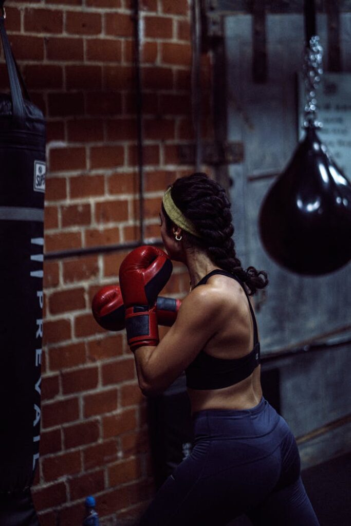 Back view of anonymous muscular female boxer in activewear and boxing gloves standing and training punches in gym